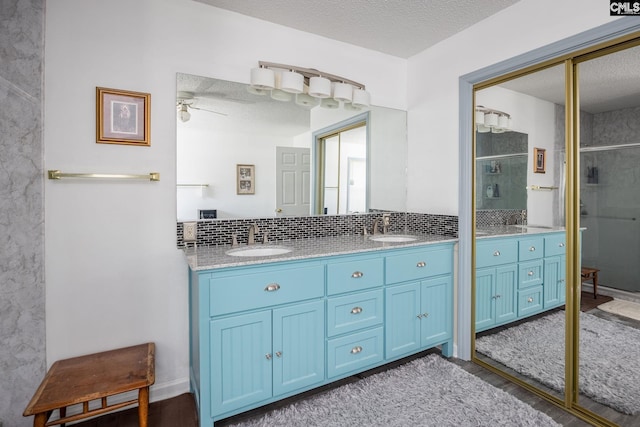 bathroom with a textured ceiling, double vanity, a sink, and a shower stall