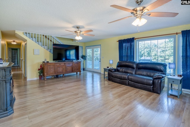 living room with light wood-type flooring, baseboards, a ceiling fan, and a textured ceiling