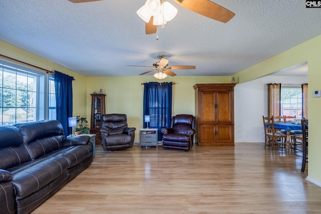 living room with baseboards, ceiling fan, light wood-style flooring, and a textured ceiling