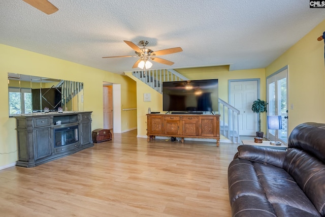 living area with light wood finished floors, baseboards, a ceiling fan, stairs, and a textured ceiling