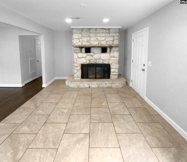 unfurnished living room with visible vents, a stone fireplace, and baseboards