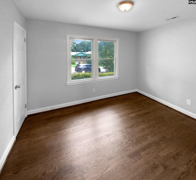 empty room with visible vents, dark wood finished floors, and baseboards