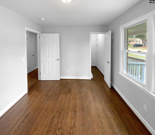 unfurnished bedroom featuring a walk in closet, a closet, dark wood finished floors, and baseboards