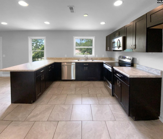 kitchen with stainless steel appliances, light countertops, a sink, and a peninsula