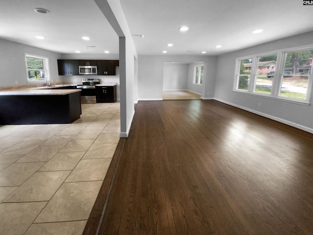 unfurnished living room featuring light wood-style floors, baseboards, a sink, and recessed lighting