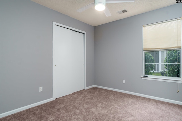 unfurnished bedroom featuring ceiling fan, a closet, a textured ceiling, and carpet flooring