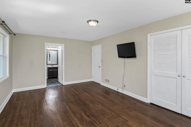 unfurnished bedroom featuring visible vents, ensuite bath, dark wood-style floors, a closet, and baseboards