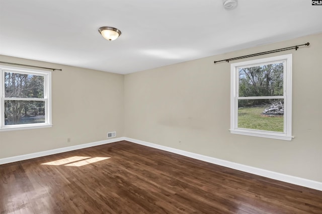 unfurnished room with dark wood-style floors, visible vents, and baseboards