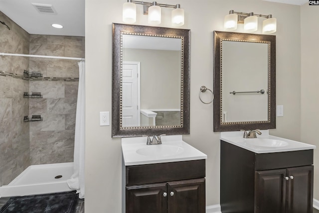 bathroom with two vanities, tiled shower, visible vents, and a sink