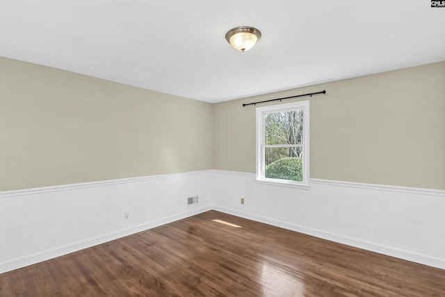 spare room with dark wood-style floors, visible vents, and baseboards