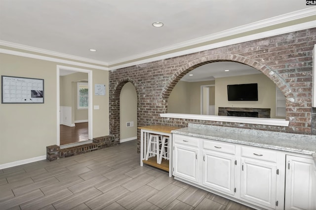 kitchen featuring wood finish floors, arched walkways, white cabinets, brick wall, and crown molding