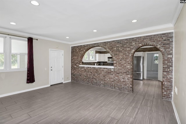 unfurnished living room featuring baseboards, arched walkways, brick wall, and ornamental molding