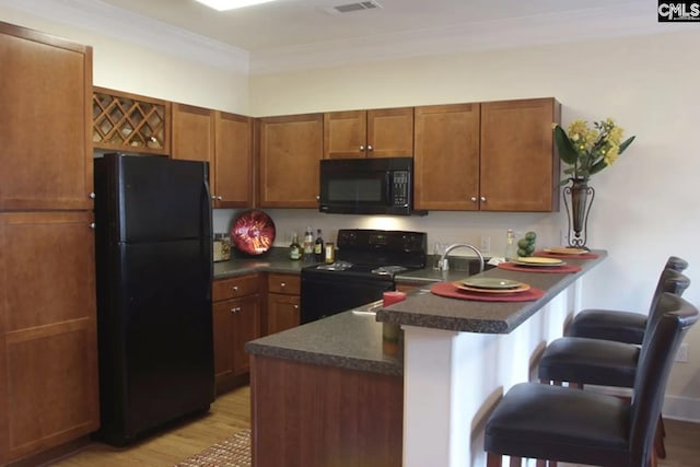 kitchen featuring light hardwood / wood-style flooring, ornamental molding, black appliances, kitchen peninsula, and a breakfast bar