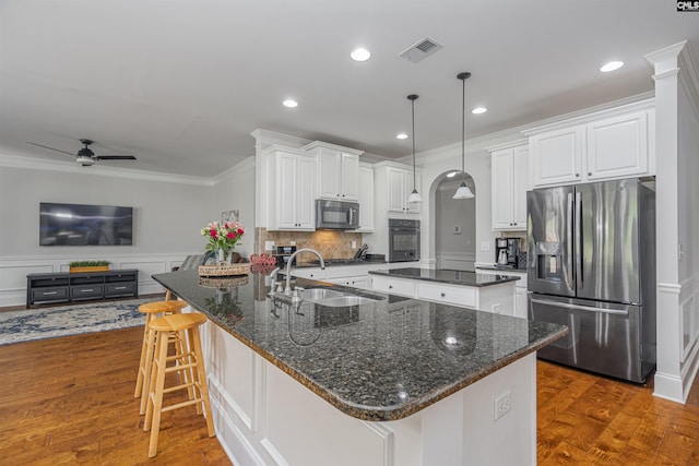 kitchen featuring stainless steel fridge, a center island with sink, white cabinets, a sink, and black oven