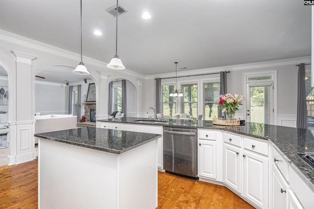 kitchen featuring arched walkways, dishwasher, ornate columns, white cabinetry, and pendant lighting