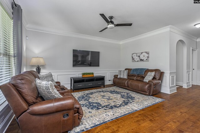 living room featuring dark wood-style floors, arched walkways, a wainscoted wall, a ceiling fan, and ornamental molding