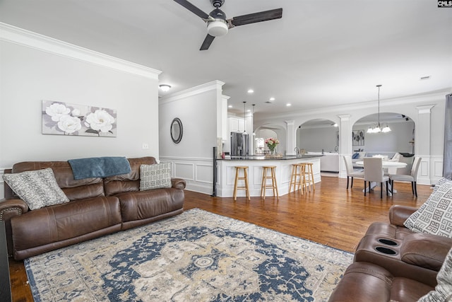 living area with arched walkways, a decorative wall, ceiling fan with notable chandelier, ornamental molding, and dark wood-style floors