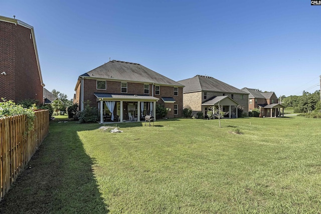 back of house featuring brick siding, a lawn, and fence