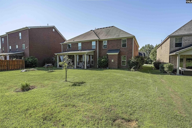 back of house with brick siding, a lawn, and fence