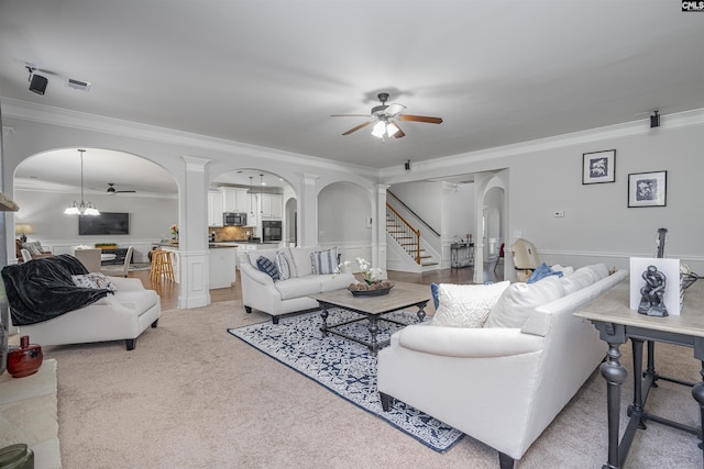 living area featuring arched walkways, ceiling fan with notable chandelier, ornamental molding, stairway, and decorative columns