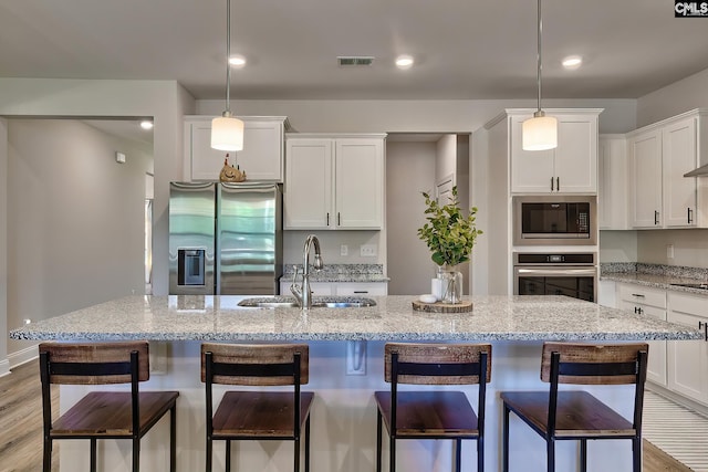 kitchen featuring decorative light fixtures, light hardwood / wood-style flooring, a kitchen island with sink, stainless steel appliances, and white cabinets