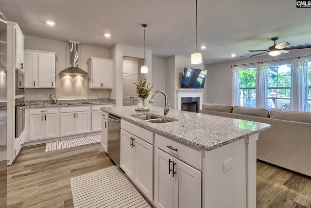 kitchen with light wood-type flooring, sink, ceiling fan, and wall chimney range hood