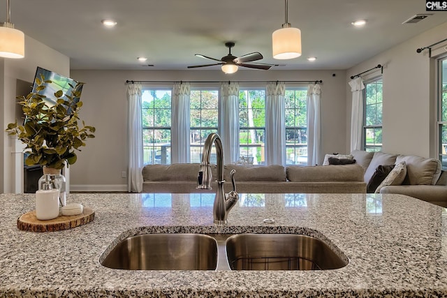 kitchen with sink, ceiling fan, light stone countertops, and a healthy amount of sunlight