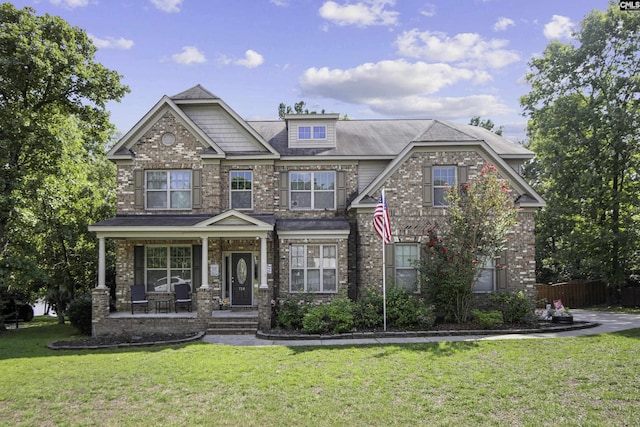 craftsman inspired home with covered porch, a front lawn, fence, and brick siding