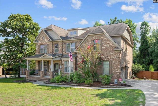 craftsman house featuring covered porch, brick siding, fence, driveway, and a front yard