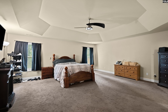 bedroom with carpet flooring, ceiling fan, a raised ceiling, and multiple windows