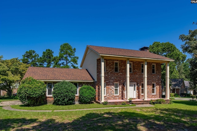 neoclassical home with brick siding, a chimney, and a front yard