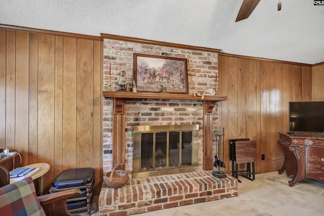 living area featuring ceiling fan, a textured ceiling, wood walls, carpet floors, and a brick fireplace