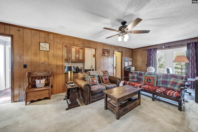 living room with ceiling fan, wooden walls, a textured ceiling, and light colored carpet