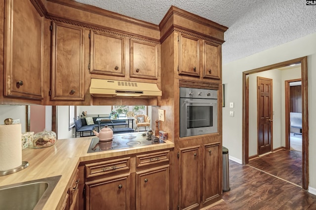 kitchen featuring dark wood-style flooring, electric stovetop, brown cabinetry, oven, and under cabinet range hood