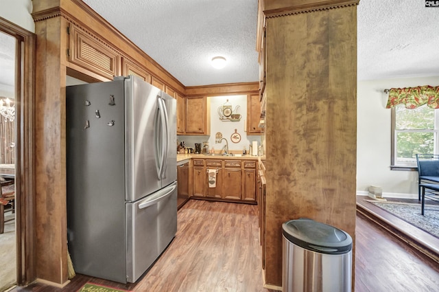 kitchen featuring a textured ceiling, light wood-style flooring, a sink, freestanding refrigerator, and brown cabinetry