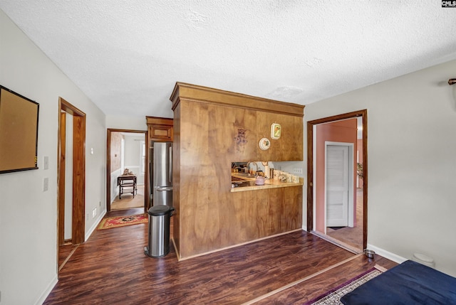 kitchen with a textured ceiling, dark wood-type flooring, freestanding refrigerator, and brown cabinets