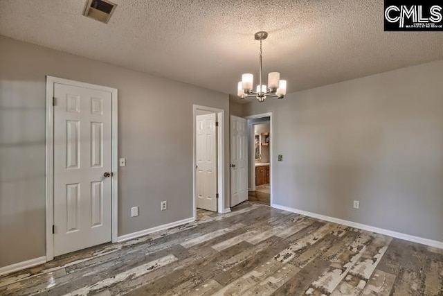 unfurnished dining area featuring a textured ceiling, an inviting chandelier, and wood-type flooring