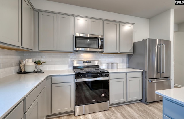 kitchen featuring decorative backsplash, gray cabinets, light wood-type flooring, and stainless steel appliances