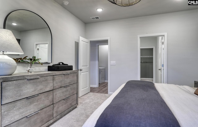 bedroom with a walk in closet, light colored carpet, and washer / dryer