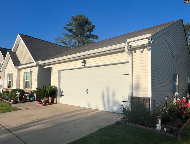 view of side of home featuring stone siding, a shingled roof, an attached garage, and driveway