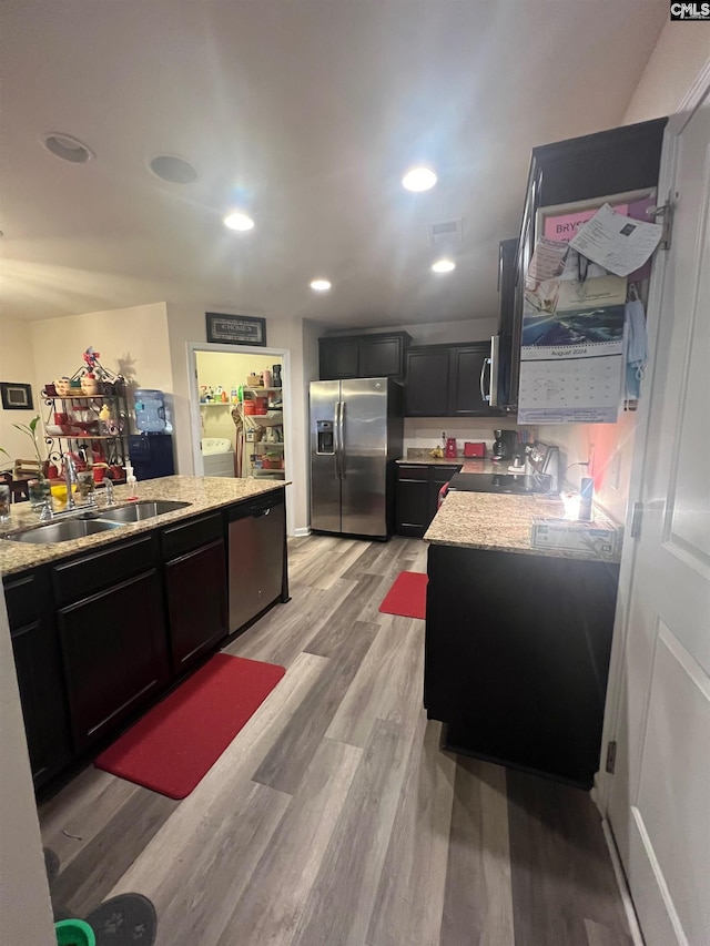 kitchen with recessed lighting, a sink, washer and dryer, appliances with stainless steel finishes, and light wood finished floors