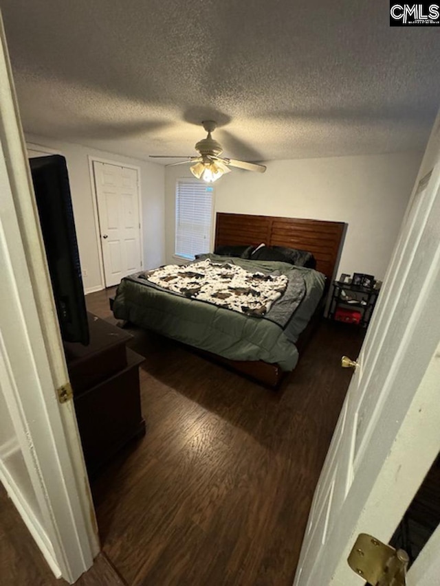 bedroom with a textured ceiling, ceiling fan, and dark wood-type flooring