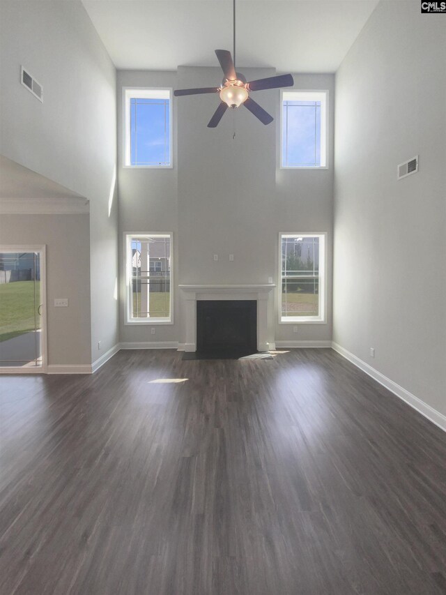 unfurnished living room with a towering ceiling, a healthy amount of sunlight, and dark hardwood / wood-style floors