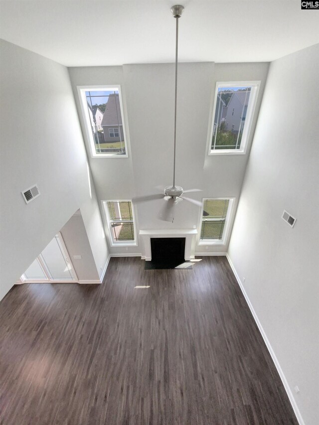 unfurnished living room featuring a healthy amount of sunlight, ceiling fan, a towering ceiling, and dark hardwood / wood-style flooring