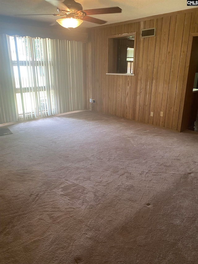 spare room featuring wooden walls, ceiling fan, and carpet