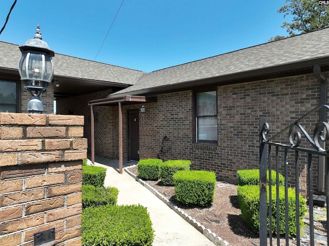 doorway to property featuring a shingled roof and brick siding