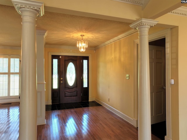 foyer featuring ornate columns, crown molding, dark wood finished floors, and baseboards
