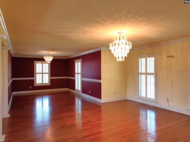 empty room featuring a chandelier, baseboards, wood finished floors, and ornamental molding