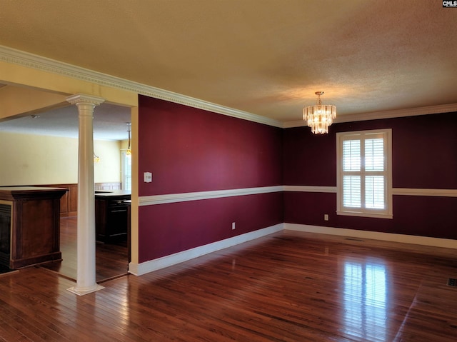 empty room with ornamental molding, decorative columns, wood finished floors, and baseboards