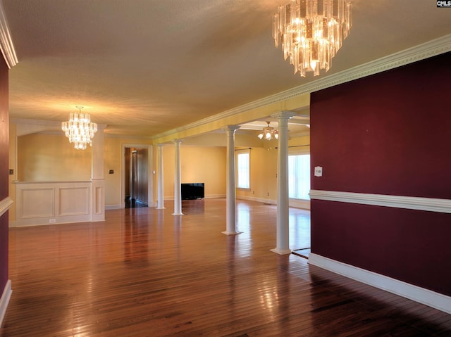 empty room with crown molding, a notable chandelier, hardwood / wood-style floors, and ornate columns